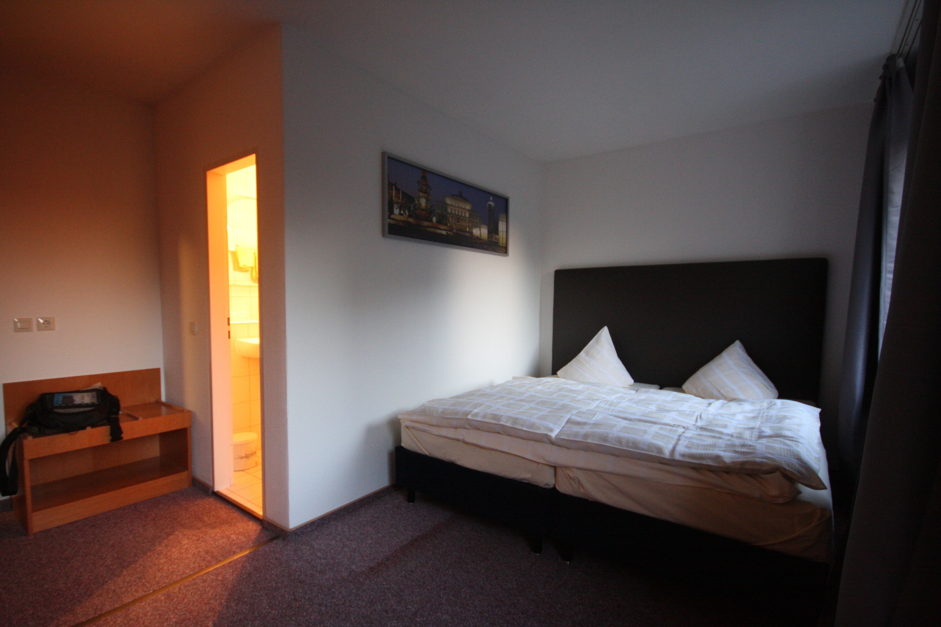 Una habitación de hotel con cama, mesita de noche, un escritorio pequeño y un cuadro en la pared.