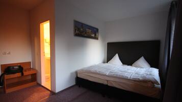 Una habitación de hotel con cama, mesita de noche, un escritorio pequeño y un cuadro en la pared.