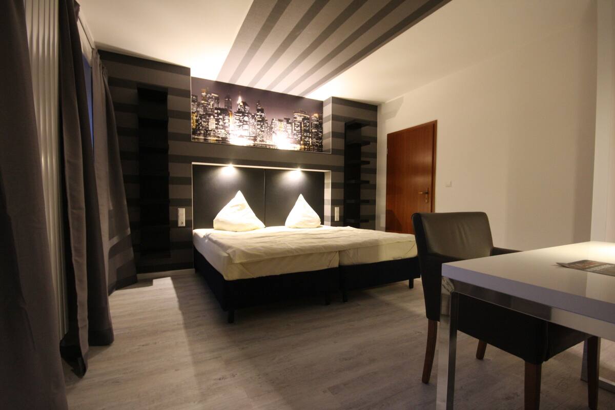 A modern bedroom with a bed, bedside lamps, a desk, and a chair.