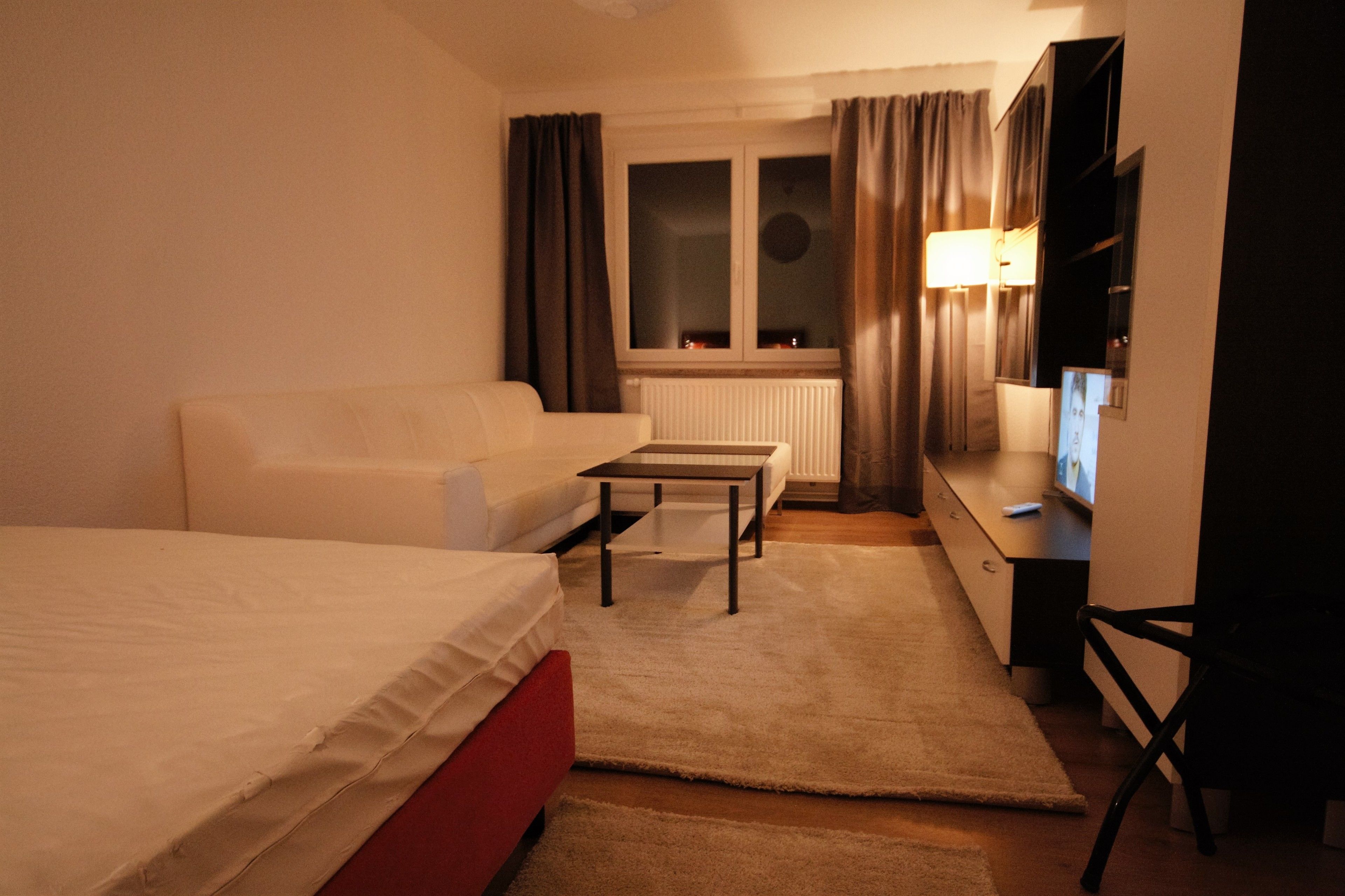 Une chambre d’hôtel avec un lit, un canapé, une petite table, une télévision et un radiateur.
