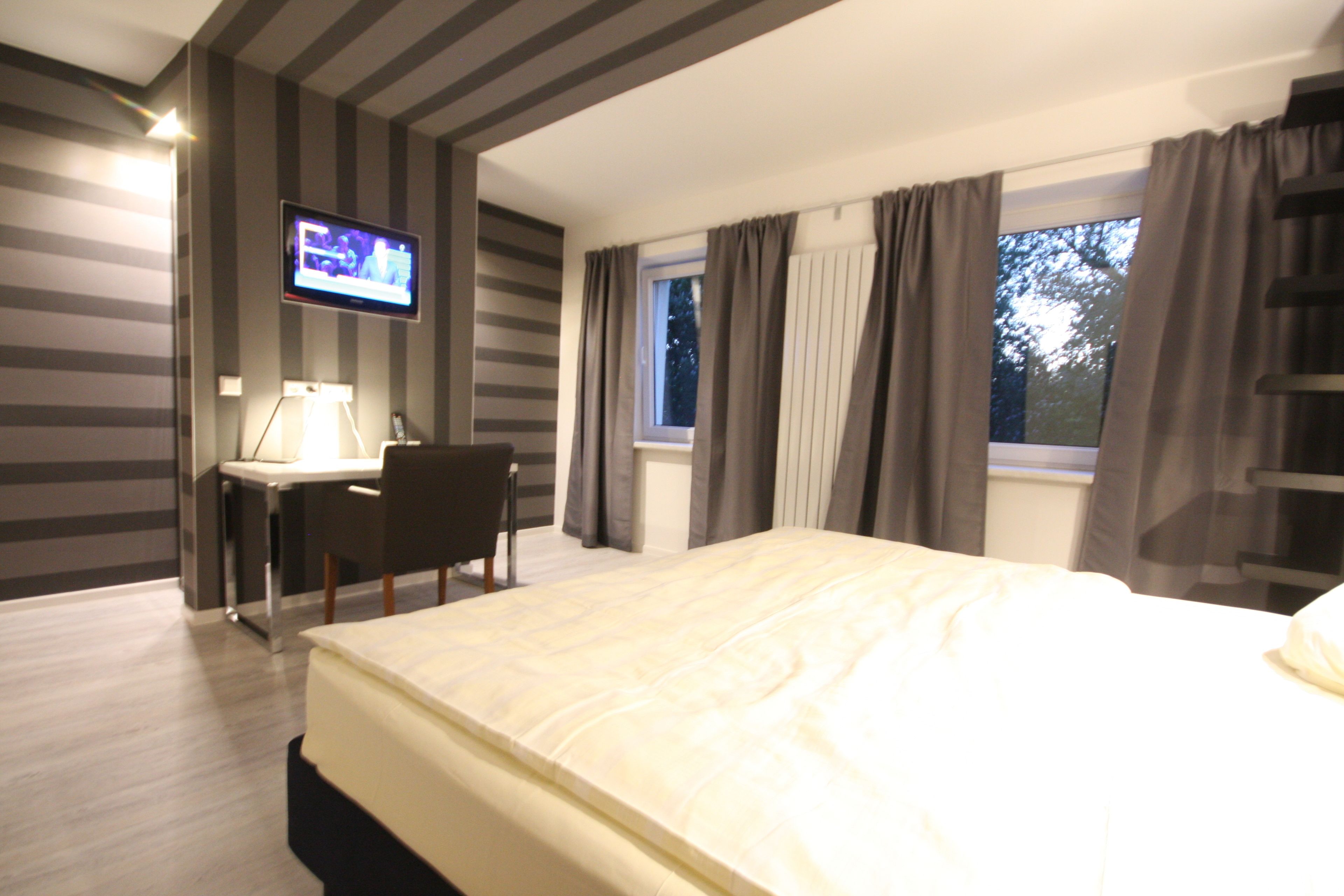 A hotel room with a bed, a desk with a chair, a television, and a window with curtains.