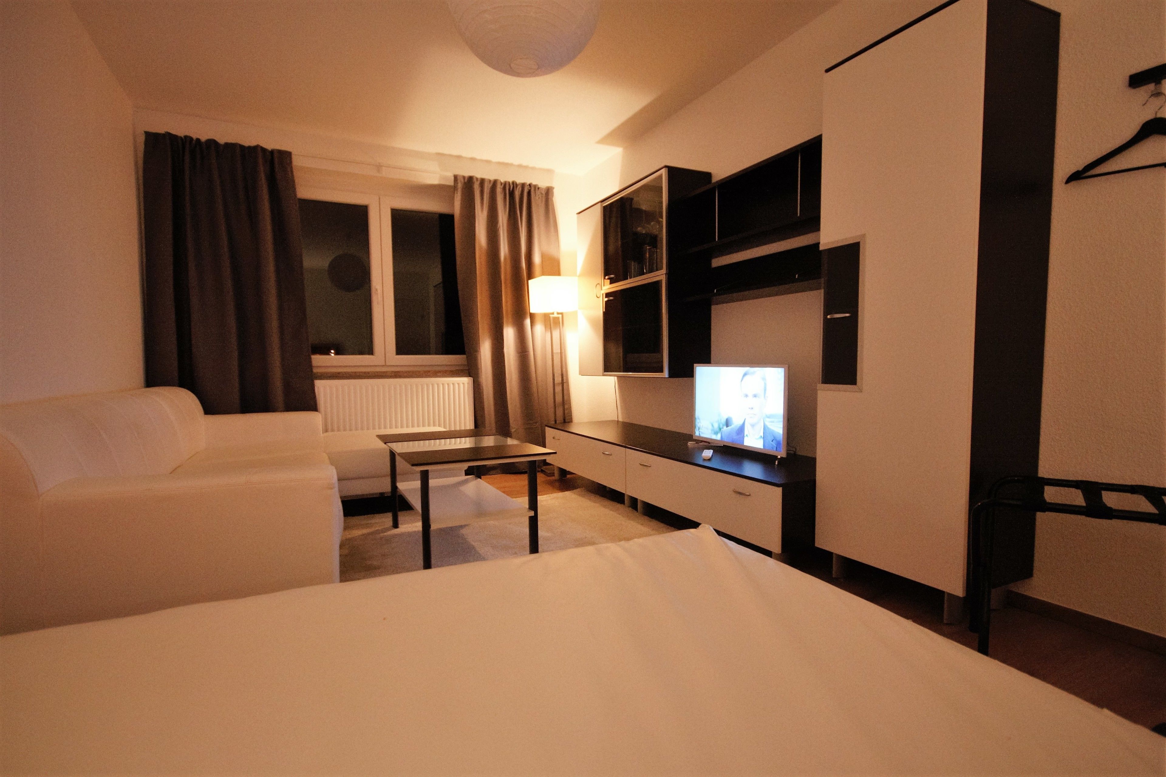 A hotel room with a bed, a sofa, a TV, a desk, and a lamp.