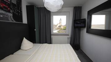 A hotel room with a bed, a television, a window with a view of a building, and a decorative ceiling light.