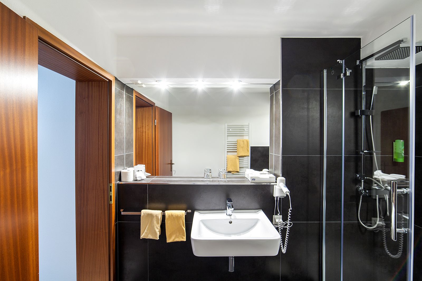 Ein modernes Badezimmer mit einem Holzlagerfläschchen, einem weißen Waschbecken, einer Duschkabine aus Glas und einem Spiegel über dem Waschbecken.