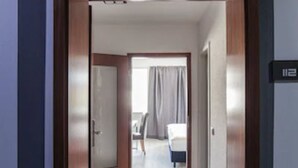 A hotel corridor with a wooden door, a bed, and a bathroom visible in the distance. - SL'otel - Budget (Bernburg)