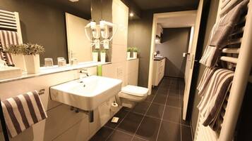 A modern bathroom with a large mirror, a sink, and a toilet. There are towels hanging on the wall and a plant on the counter.