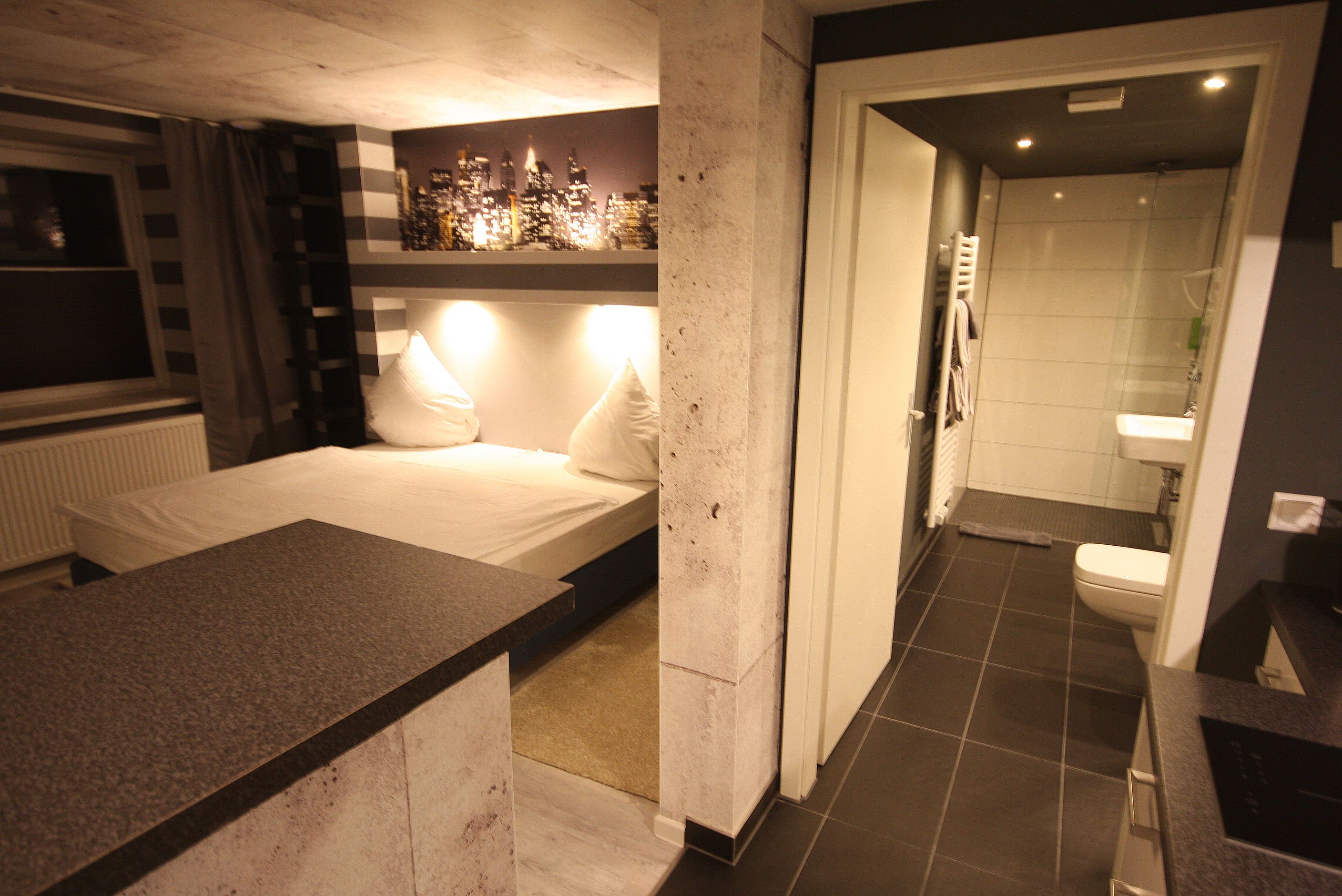 Un dormitorio moderno con cama, vistas a la ciudad, baño con inodoro y lavamanos, y ducha.