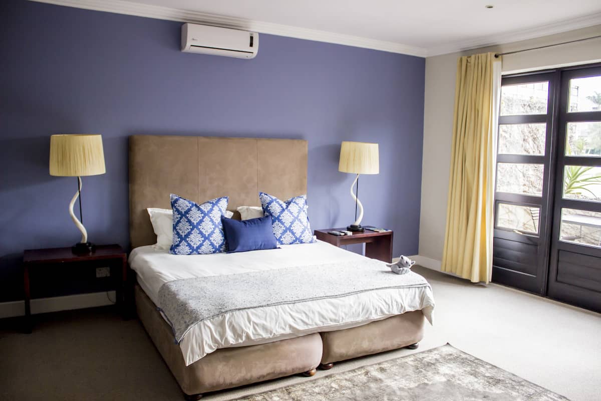 A bedroom with a large bed, two nightstands, a lamp on each, and a view through a door.