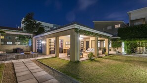 Un patio extérieur couvert, aménagé avec des sièges et un foyer, entouré d’une pelouse bien entretenue et d’un chemin pavé.
