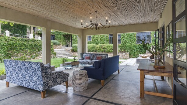 Un espace extérieur aménagé avec un coin salon abrité, comprenant un canapé à motifs, un canapé bleu et une table en bois.