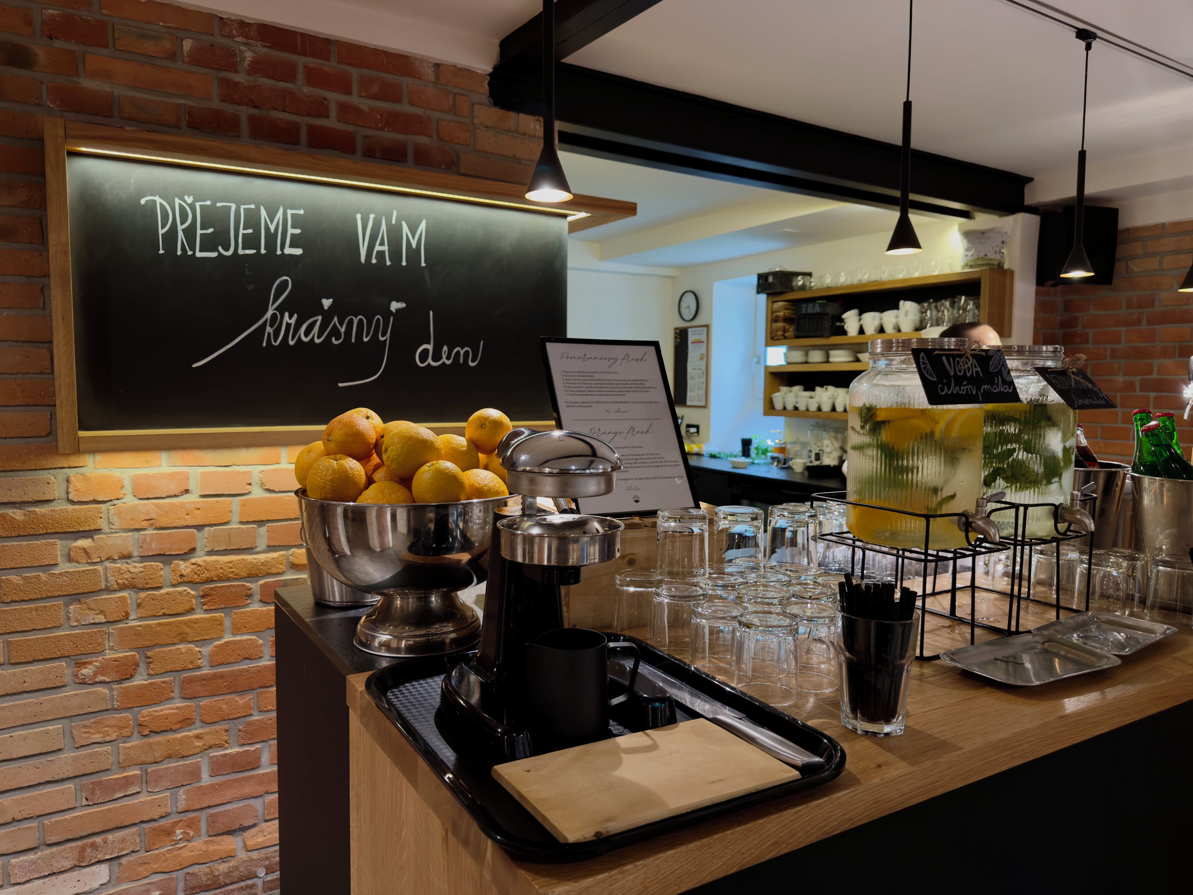 Un espace bar avec un tableau noir servant de menu, un panier de fruits et une machine à café.