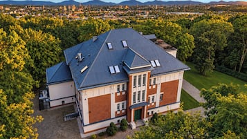 Un grand bâtiment à deux étages, doté d’un toit plat et de nombreuses fenêtres, entouré d’une végétation luxuriante et surplombant un ciel dégagé.