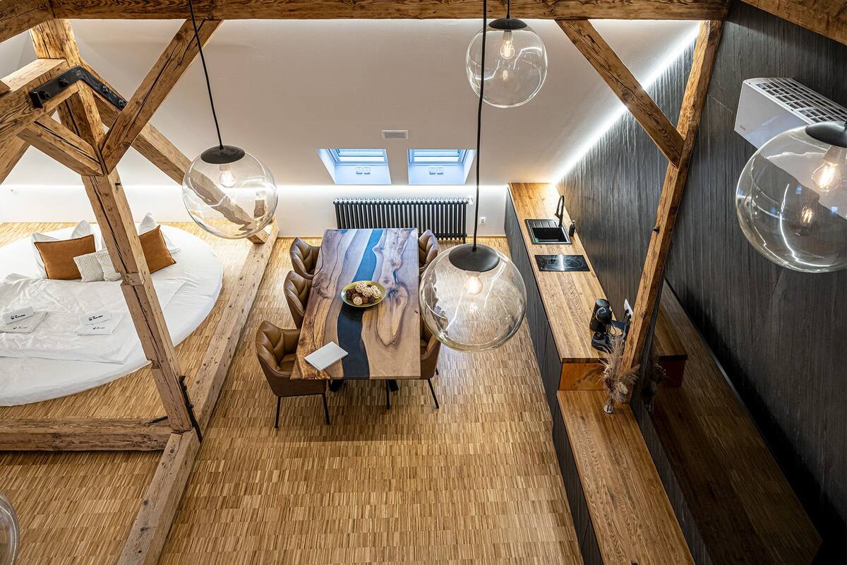 Un intérieur moderne avec une structure de plafond en bois, une table à manger centrale entourée de chaises et des luminaires suspendus.