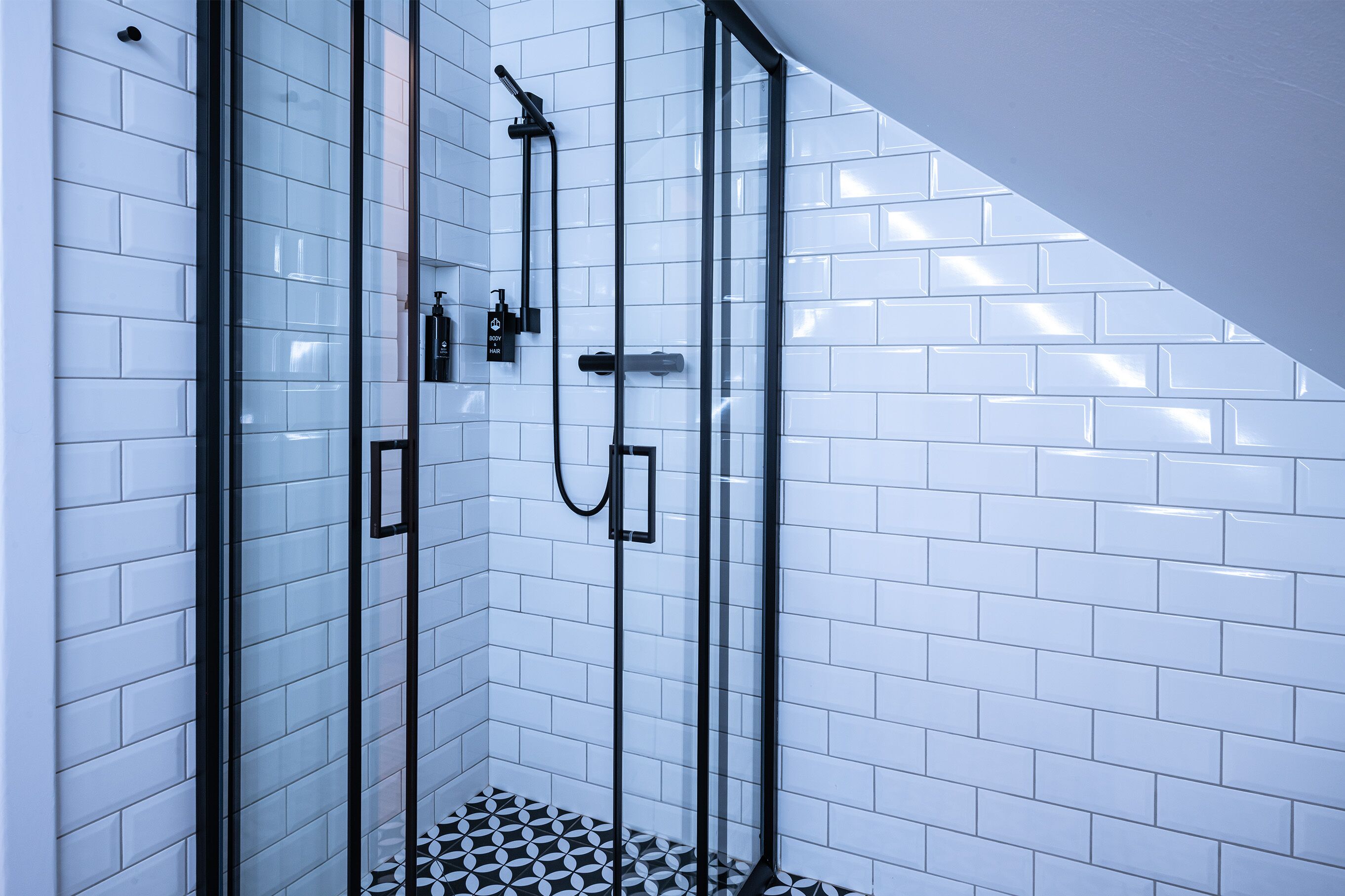 Un área de ducha moderna con puertas de cristal y paredes de azulejos blancos.