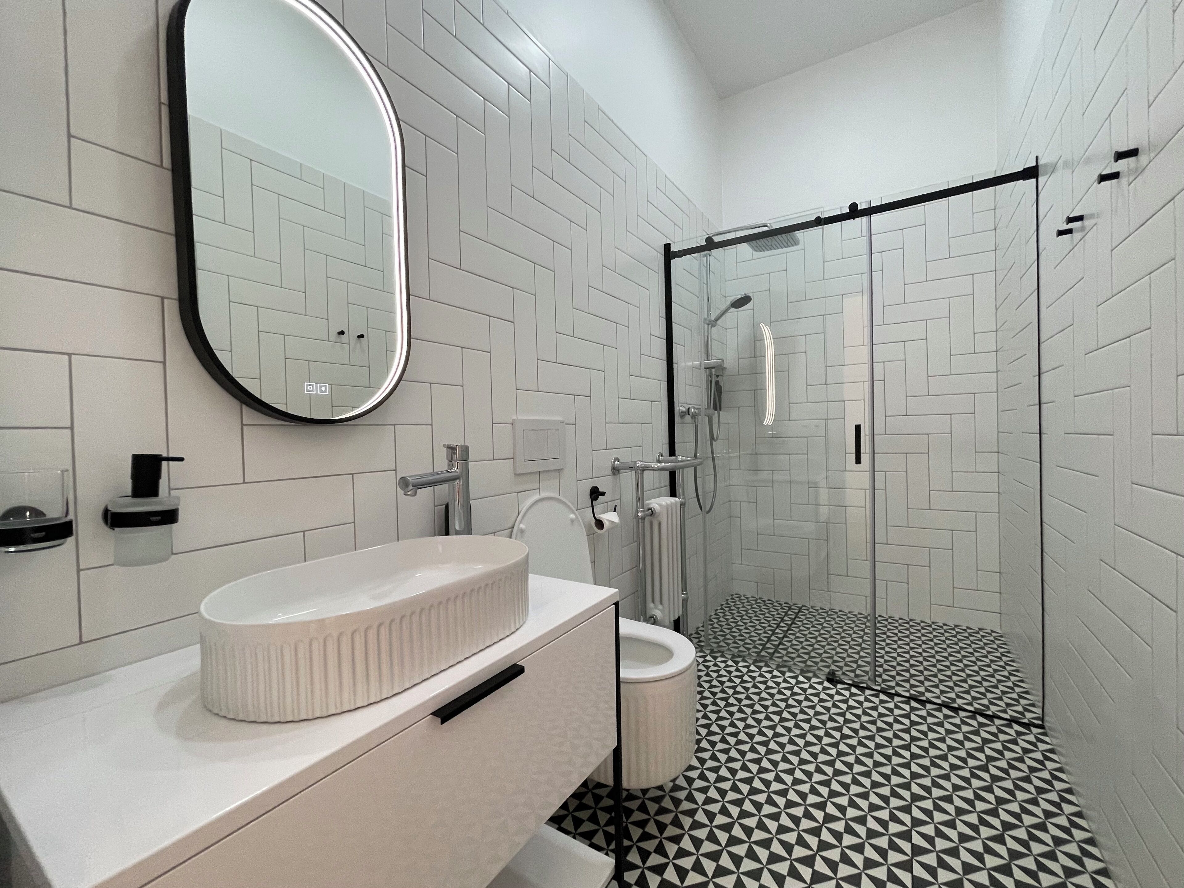 Un baño moderno con un tocador blanco, un espejo redondo, un inodoro y una zona de ducha.