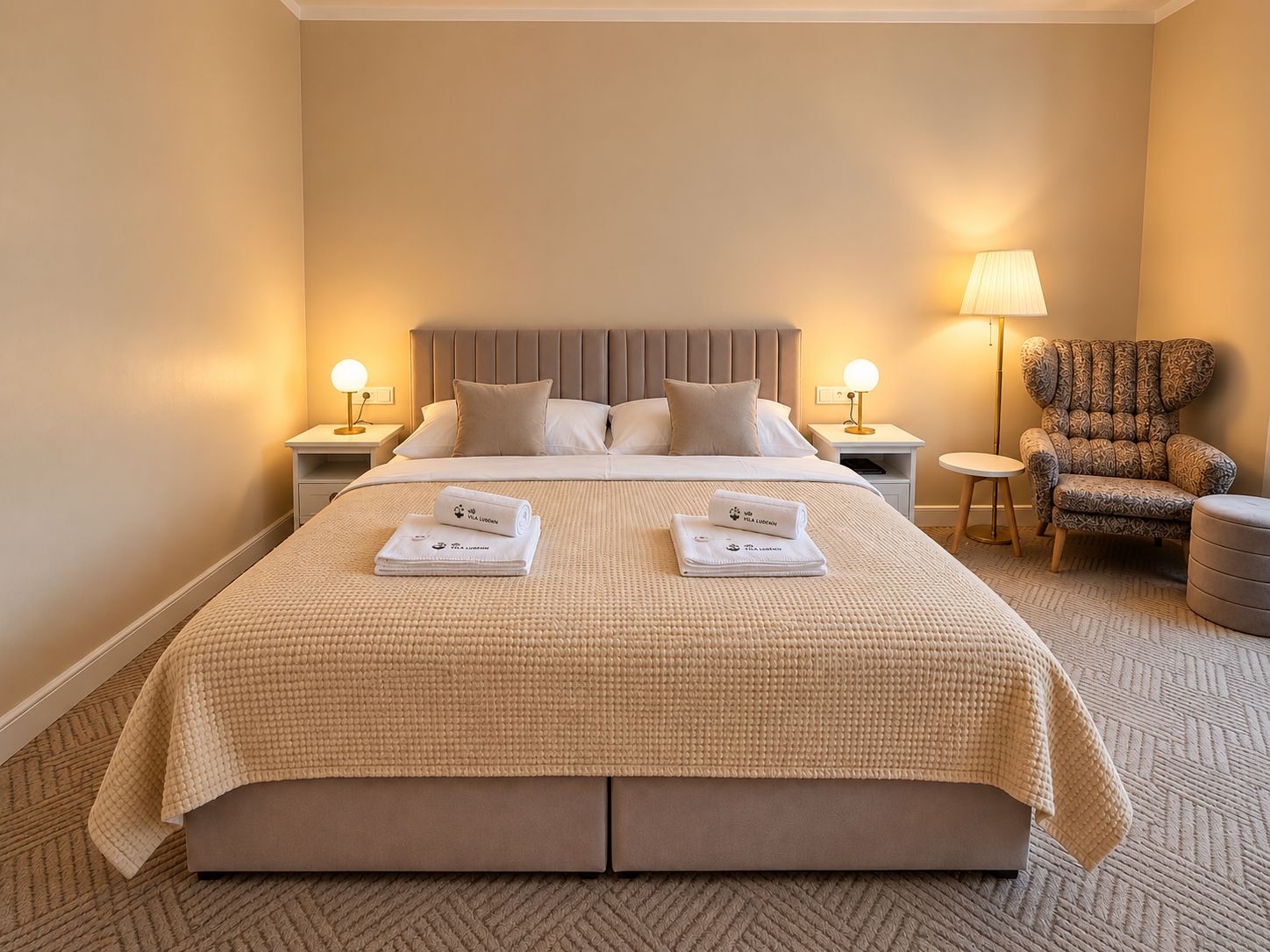 Habitación de hotel con una cama grande, dos mesitas de noche, una silla y una lámpara.