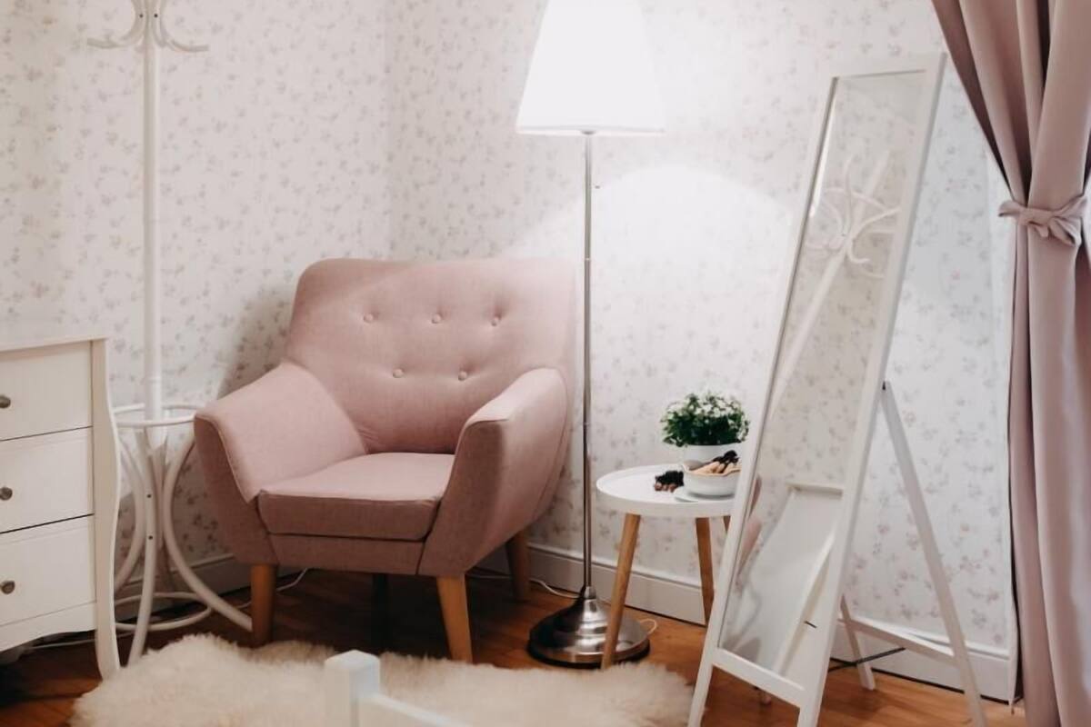 Une pièce avec un fauteuil rose, une lampe sur pied, une petite table avec une plante et un grand miroir.
