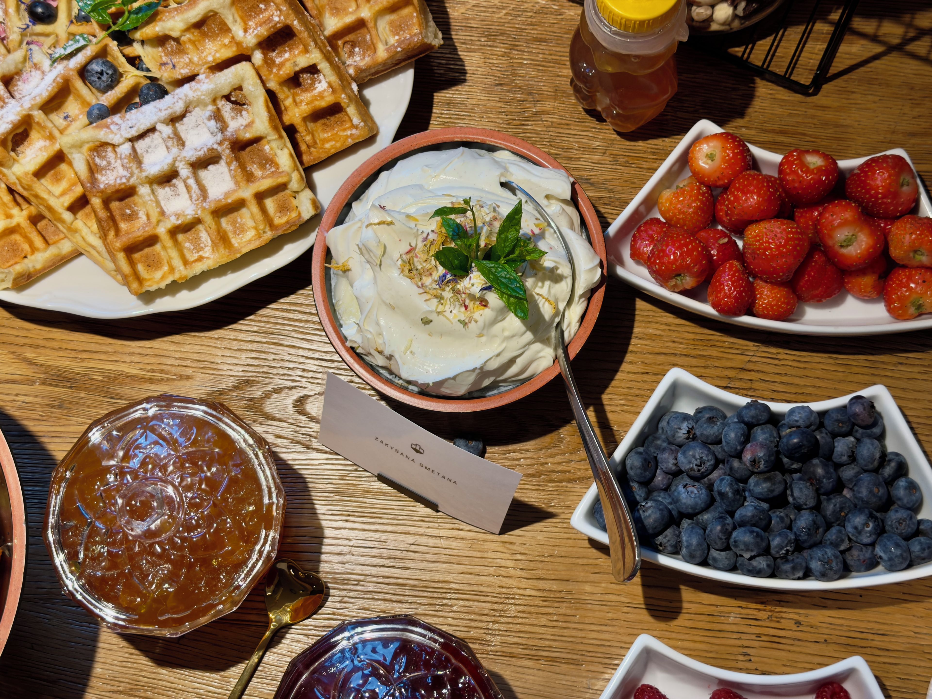 Una mesa con waffles, fresas, arándanos y un tazón de yogur con menta.