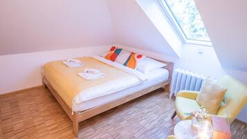 A bedroom with a wooden bed, a yellow armchair, a small table with a lamp, and a skylight.