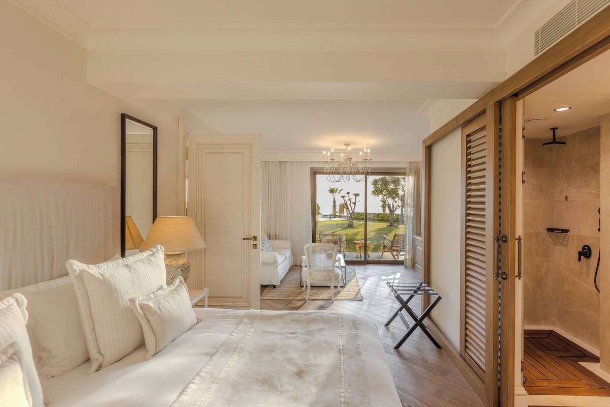 A hotel room with a bed, a sitting area with a chair and a table, a mirror, and a view of the outdoors.