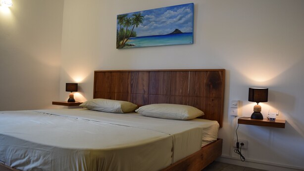 Une chambre à coucher avec un lit en bois, deux tables de chevet avec des lampes, un tableau représentant un paysage tropical et une petite table de nuit avec une lampe.