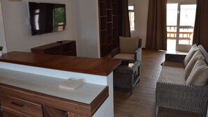 Un salon moderne doté d’un téléviseur à écran plat, de meubles en bois, de canapés en osier et d’une porte-fenêtre coulissante donnant sur un espace extérieur.