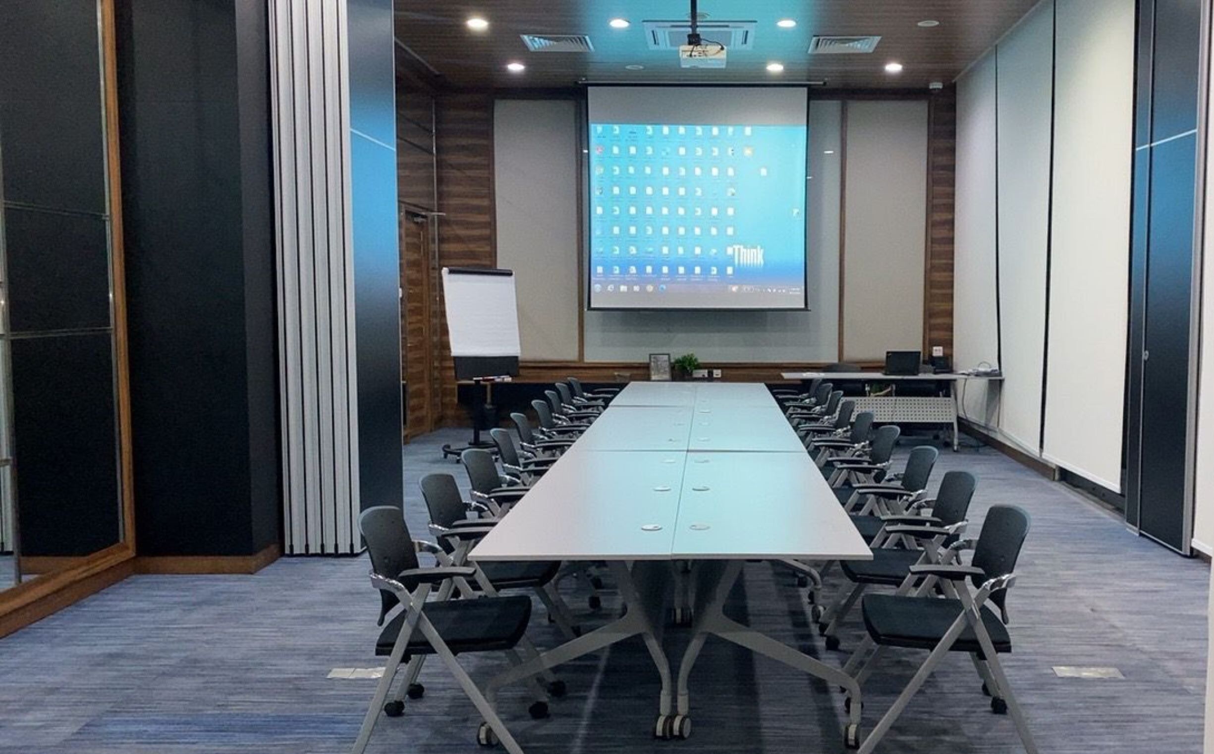Une salle de conférence équipée d’une longue table, de chaises, d’un écran de projection et d’un tableau blanc.