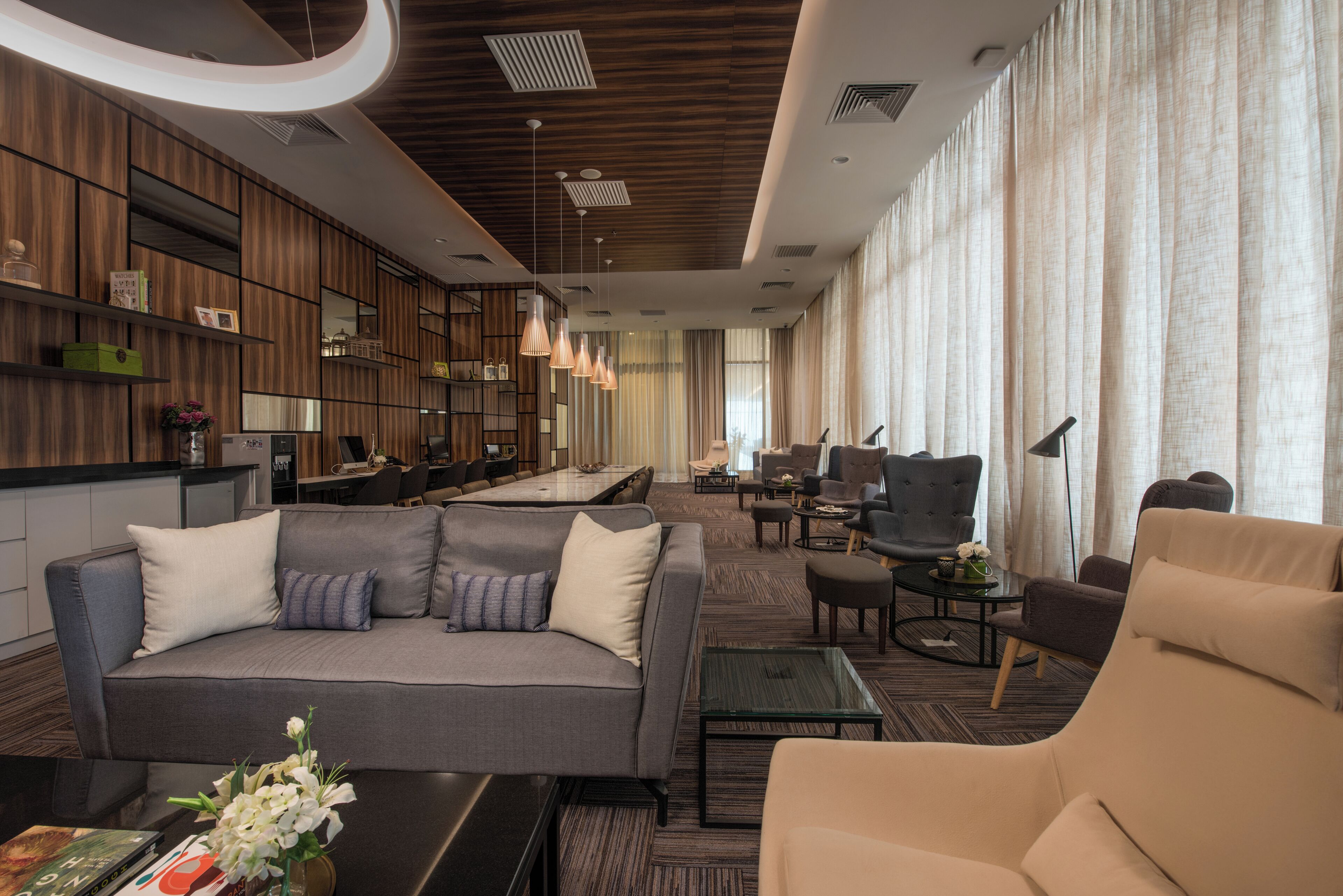 A modern hotel lobby with a grey sofa, armchairs, a coffee table, and a bookshelf.