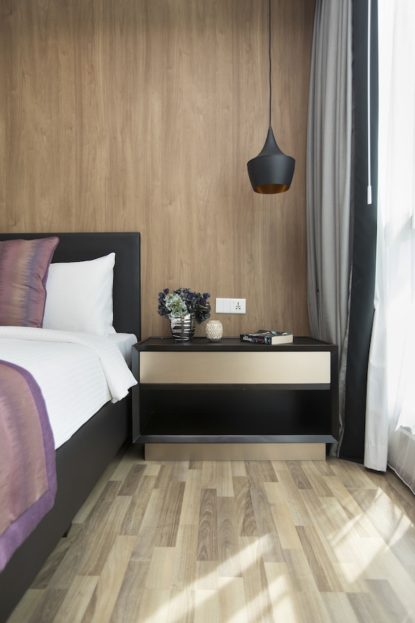 Ein modernes Schlafzimmer mit einer Holzwand, einem Bett mit weißer Bettwäsche, einem Nachttisch mit Blumenvasen und einer hängenden Pendelleuchte.