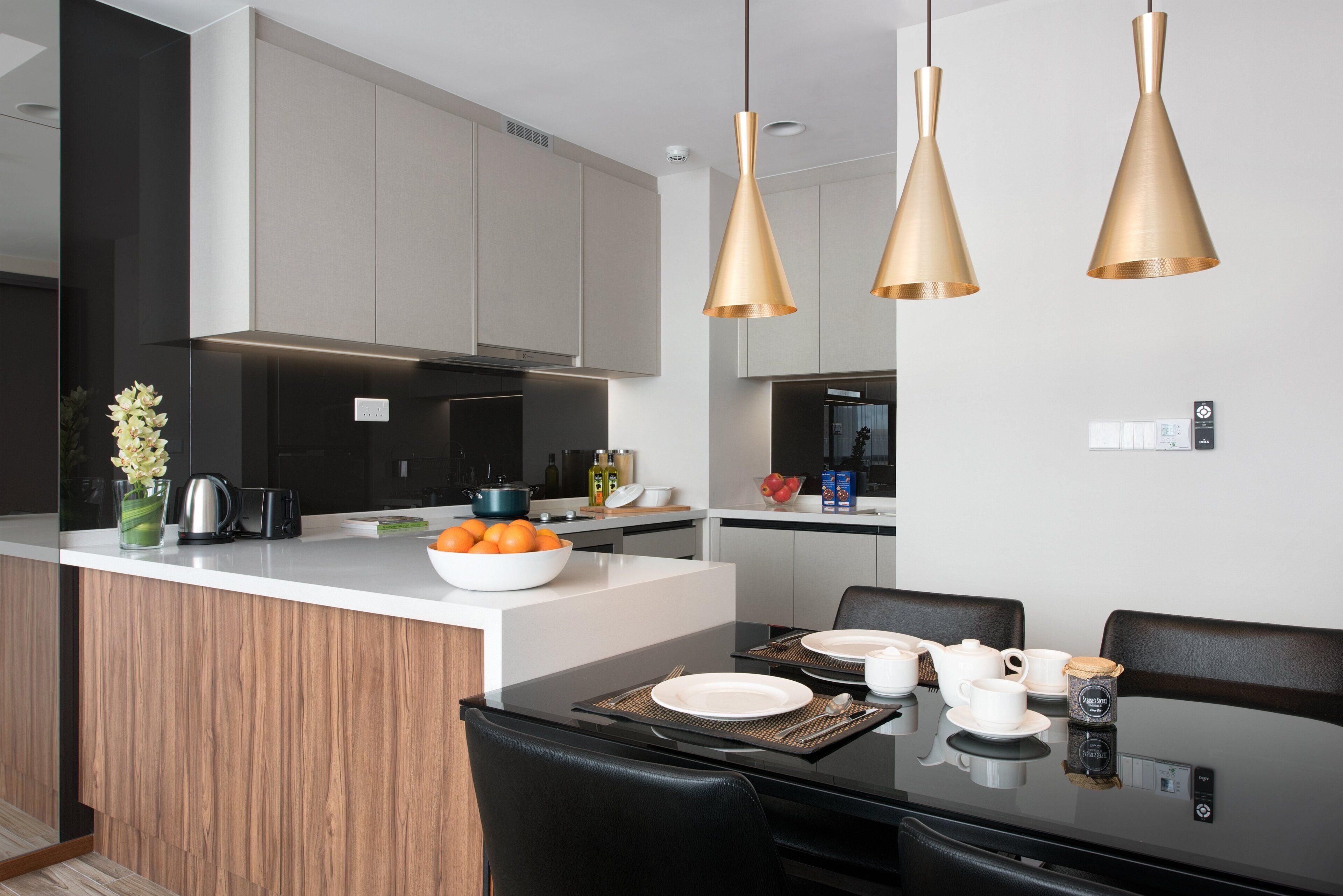 Una cocina moderna con una isla central, iluminación colgante y un comedor con mesa y sillas negras.