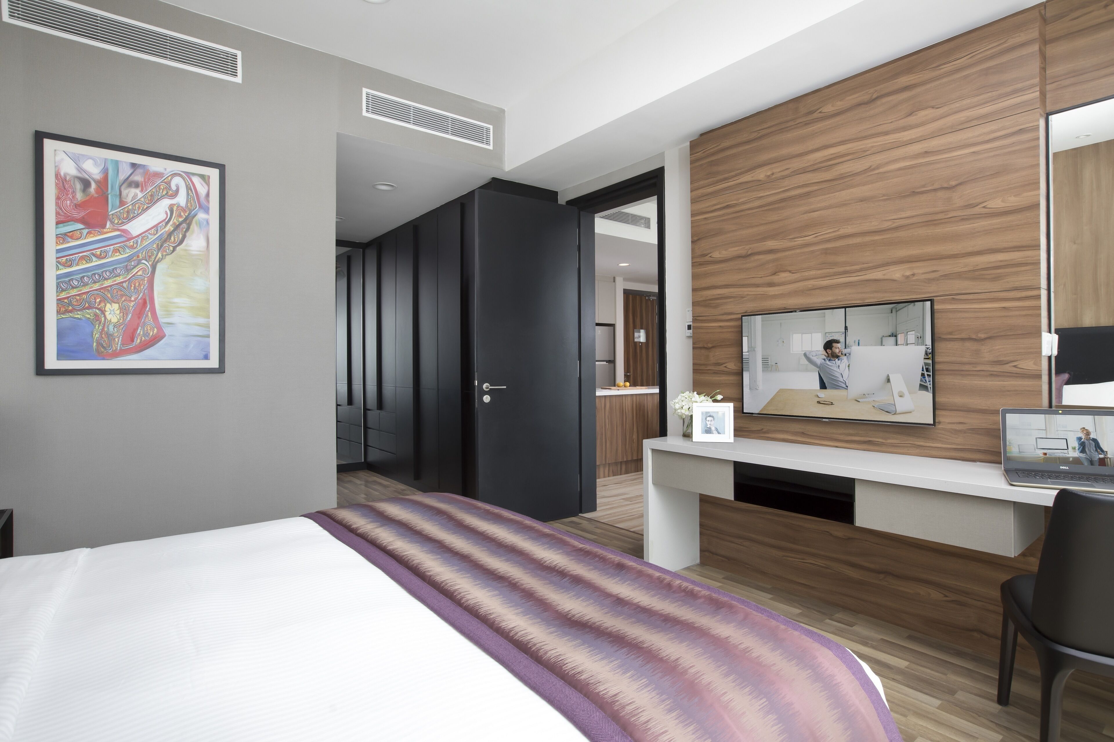 A modern hotel room with a large bed, a desk with a laptop, a television, and a wooden accent wall.