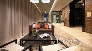 A modern living room with a brown leather sofa, black and white patterned cushions, a glass coffee table with a magazine and a green drink, and a large window with a view of the city. - Somerset Damansara Utama Petaling Jaya (Petaling Jaya)