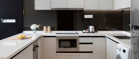 Una cocina moderna con armarios de colores claros, horno empotrado, microondas, lavadora y encimera con un jarrón de flores.