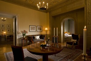 Een luxueuze kamer met een ronde eettafel, een bank, een kroonluchter en een bed met hemelbed.