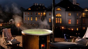 Un bain à remous avec jets de vapeur, entouré de chaises longues, devant un grand bâtiment doté de nombreuses fenêtres et d’une cheminée.