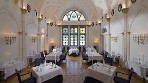 Une salle à manger avec des tables dressées, un plafond voûté et des vitraux.
