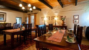 A dining area with wooden tables and chairs, a chandelier, and framed pictures on the walls. - Leeuwenbosch Shearers Lodge (Paterson)