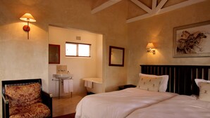 A bedroom with a bed, a chair, a nightstand, a bedside table, a wall-mounted lamp, a window, a mirror, and a painting. - Leeuwenbosch Shearers Lodge (Paterson)