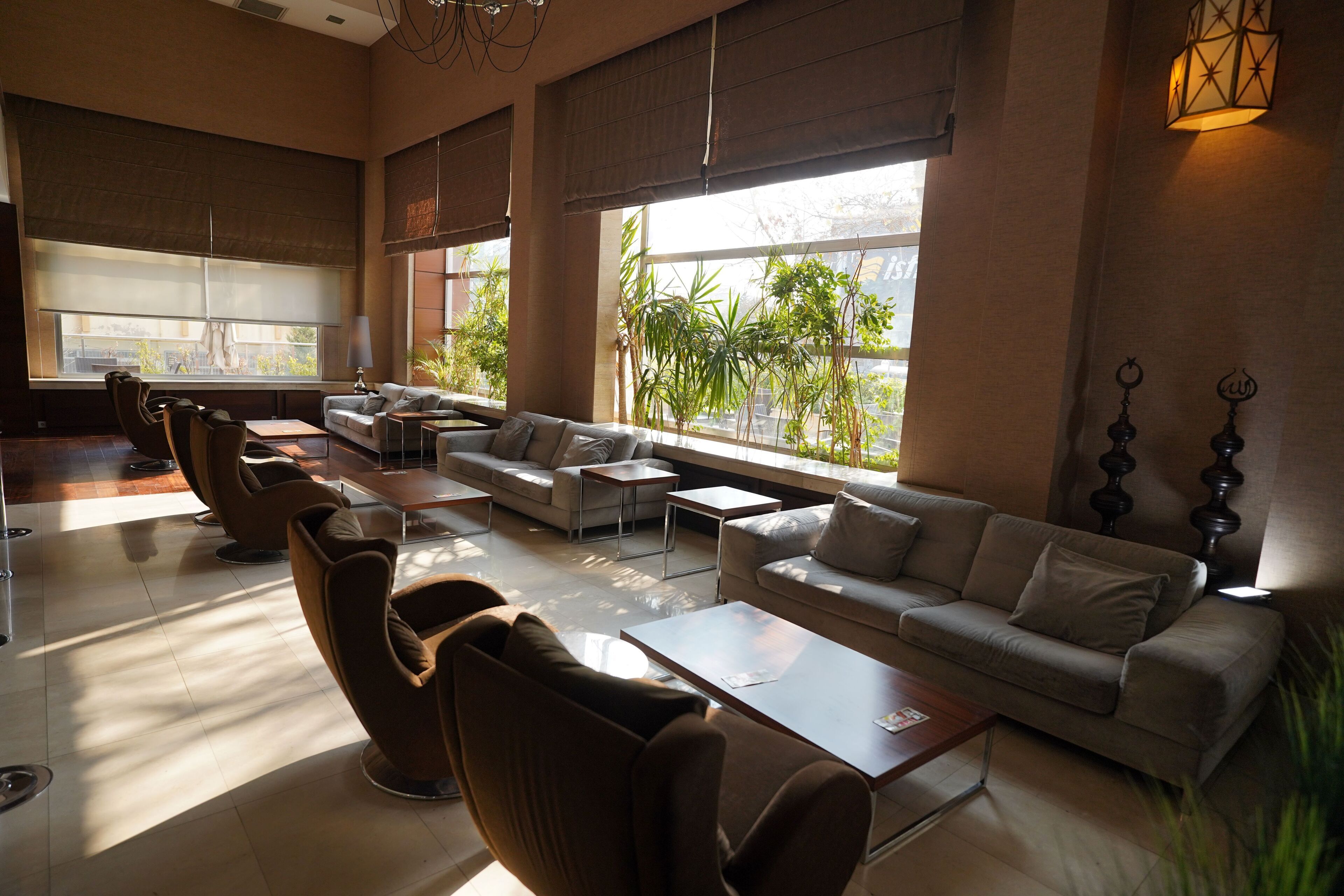 Amplia sala de estar con diversas opciones de asientos, incluyendo sofás y sillones, grandes ventanales que ofrecen vistas al exterior, y una lámpara moderna.