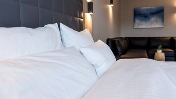 A modern hotel room with a large bed, a dark headboard, and a black leather sofa.