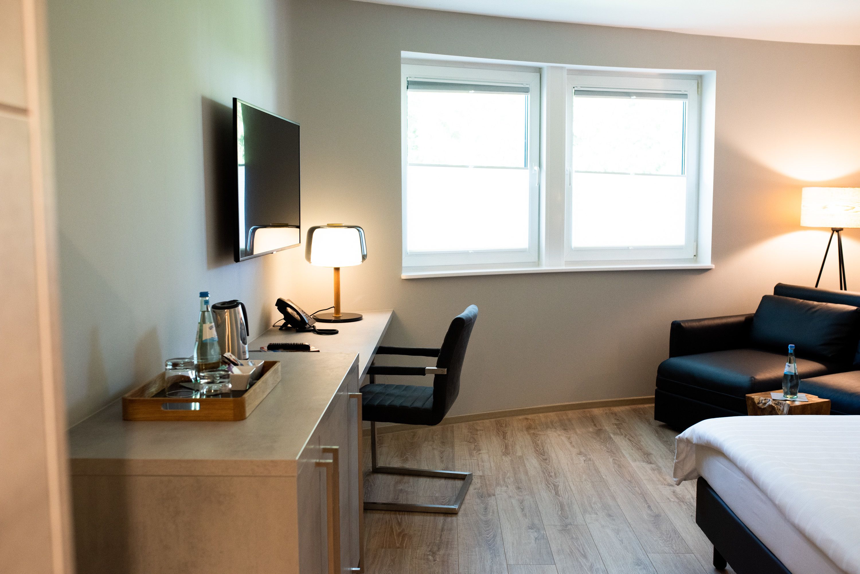 A hotel room with a desk, chair, bed, and a TV mounted on the wall.