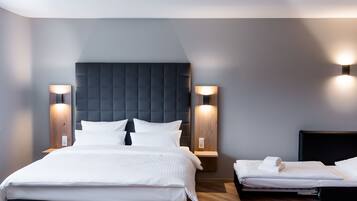 Una habitación de hotel moderna con una cama grande, dos mesitas de noche con lámparas, un cabecero de madera y una pequeña mesita de noche con una toalla.