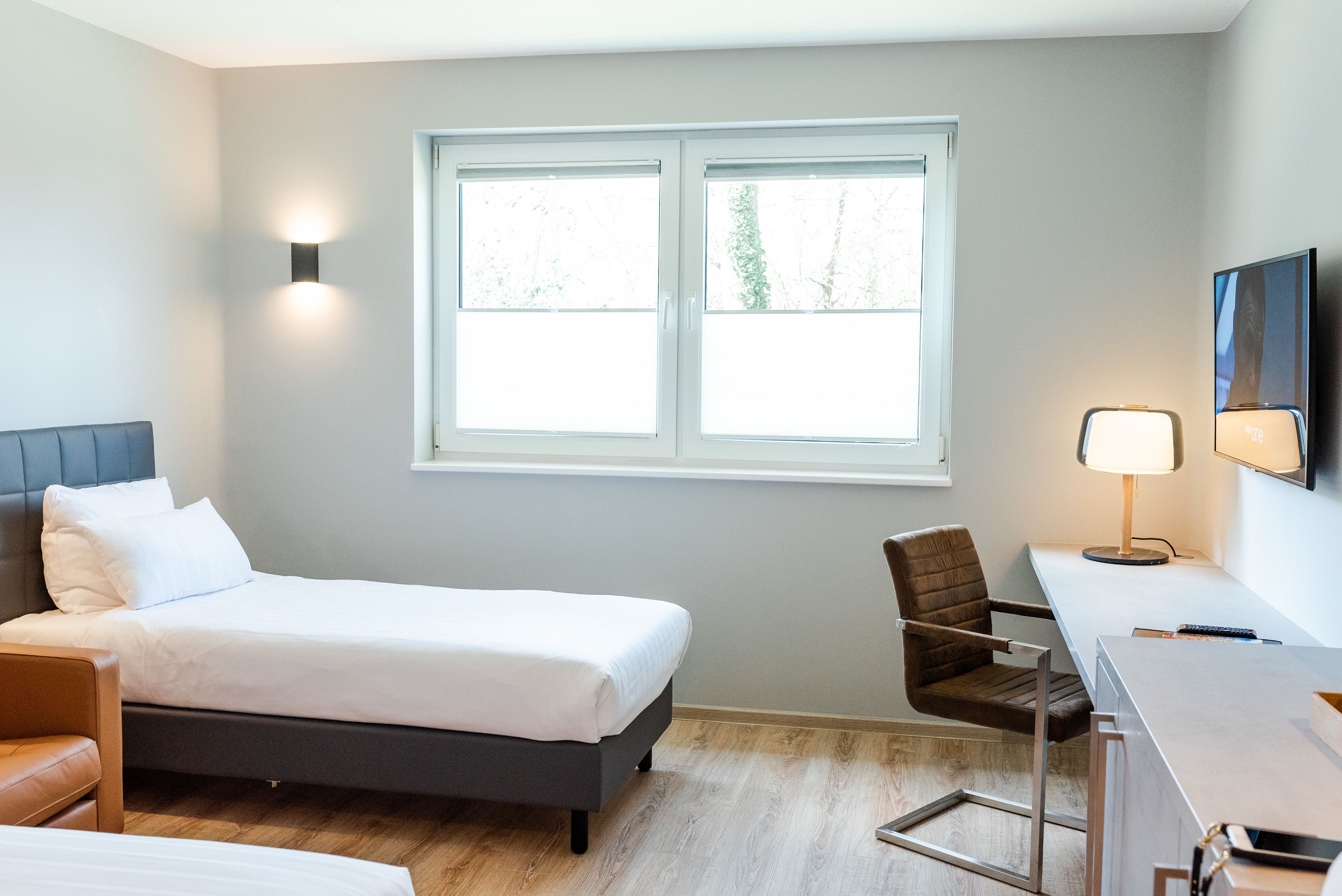 Una habitación de hotel moderna con una cama, un escritorio, una silla y una ventana con vistas a árboles.