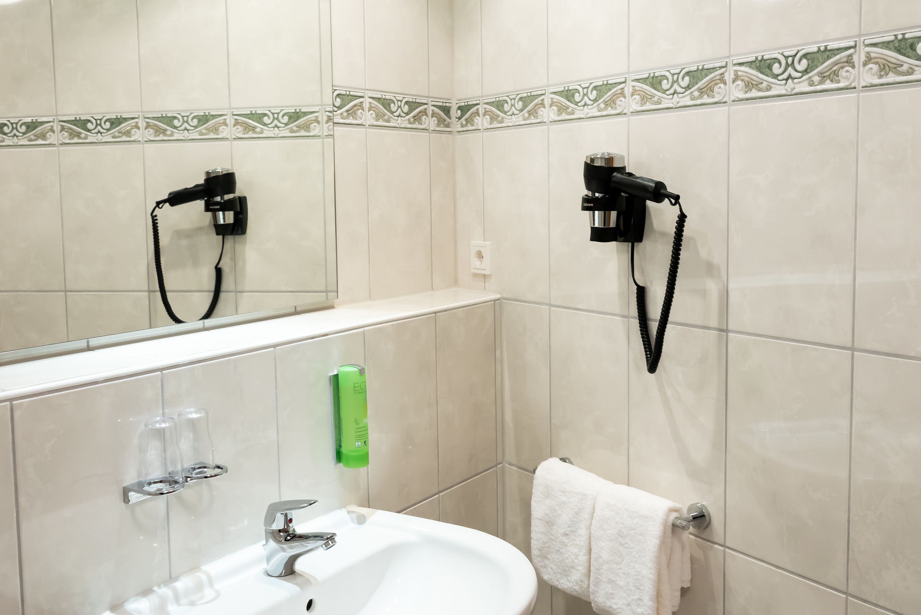 A bathroom with a sink, mirror, towel rack, and hairdryer mounted on the wall.