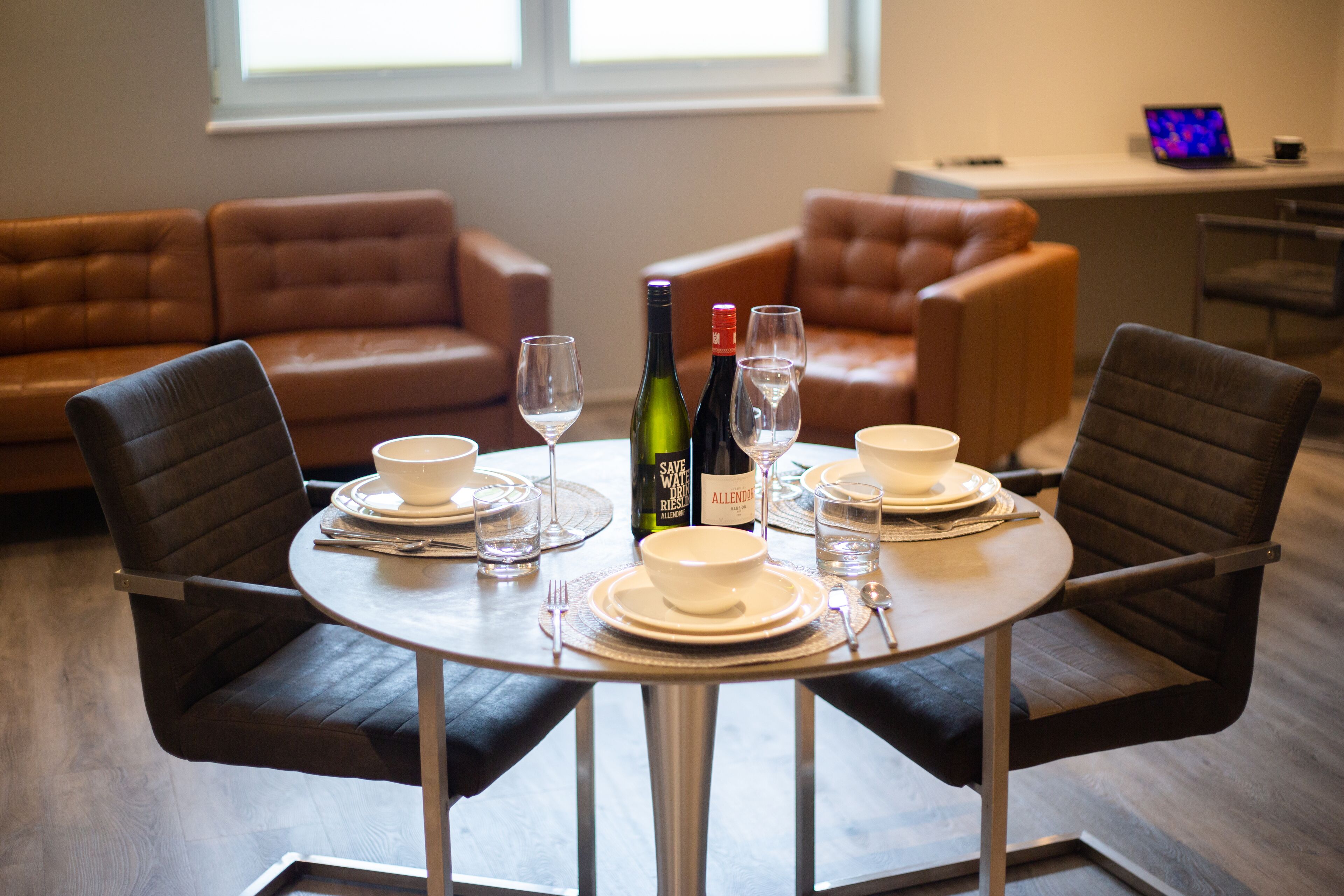 A dining area with a round table set for four, surrounded by leather sofas.