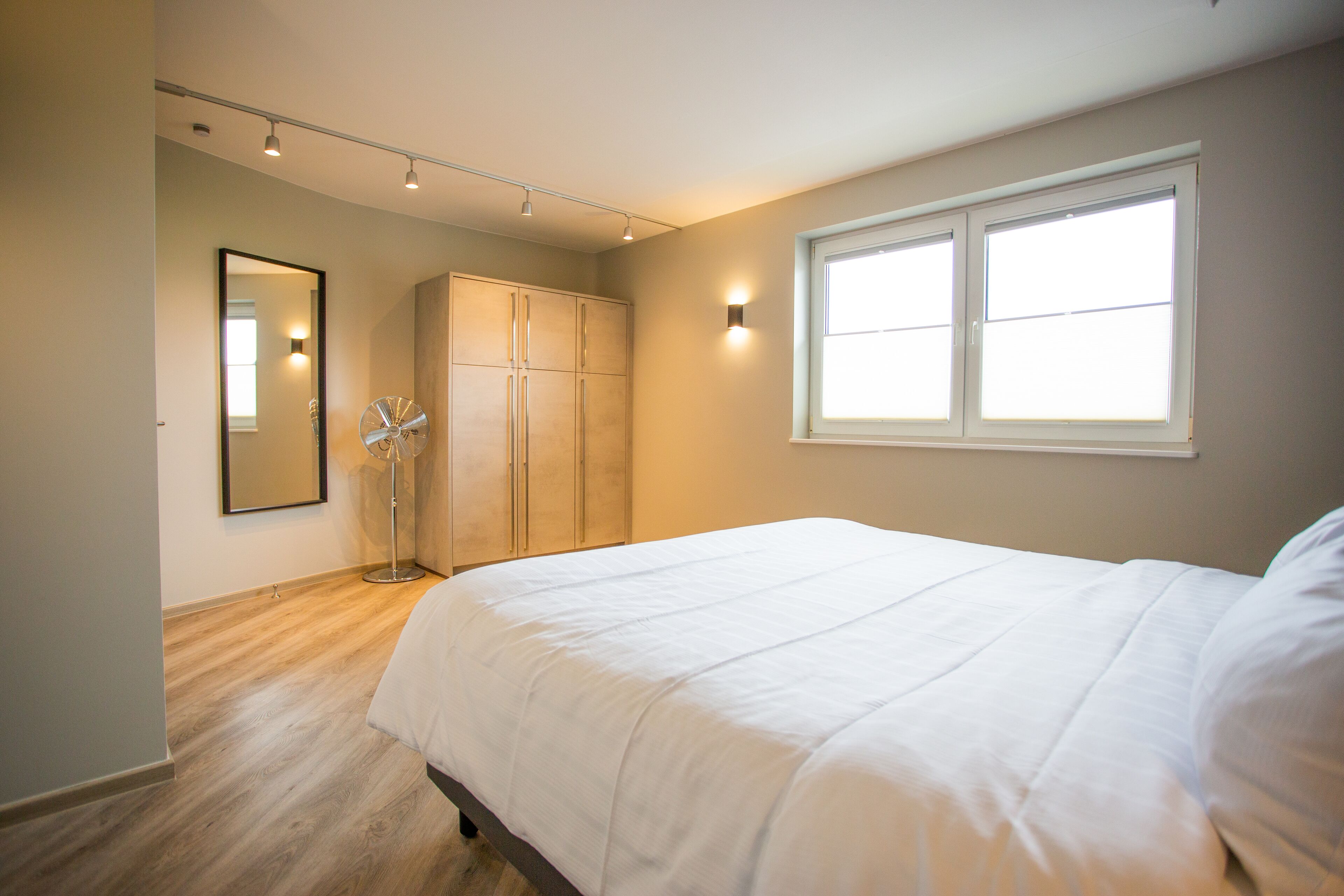 Un dormitorio con una cama grande, un armario, un espejo y una ventana.