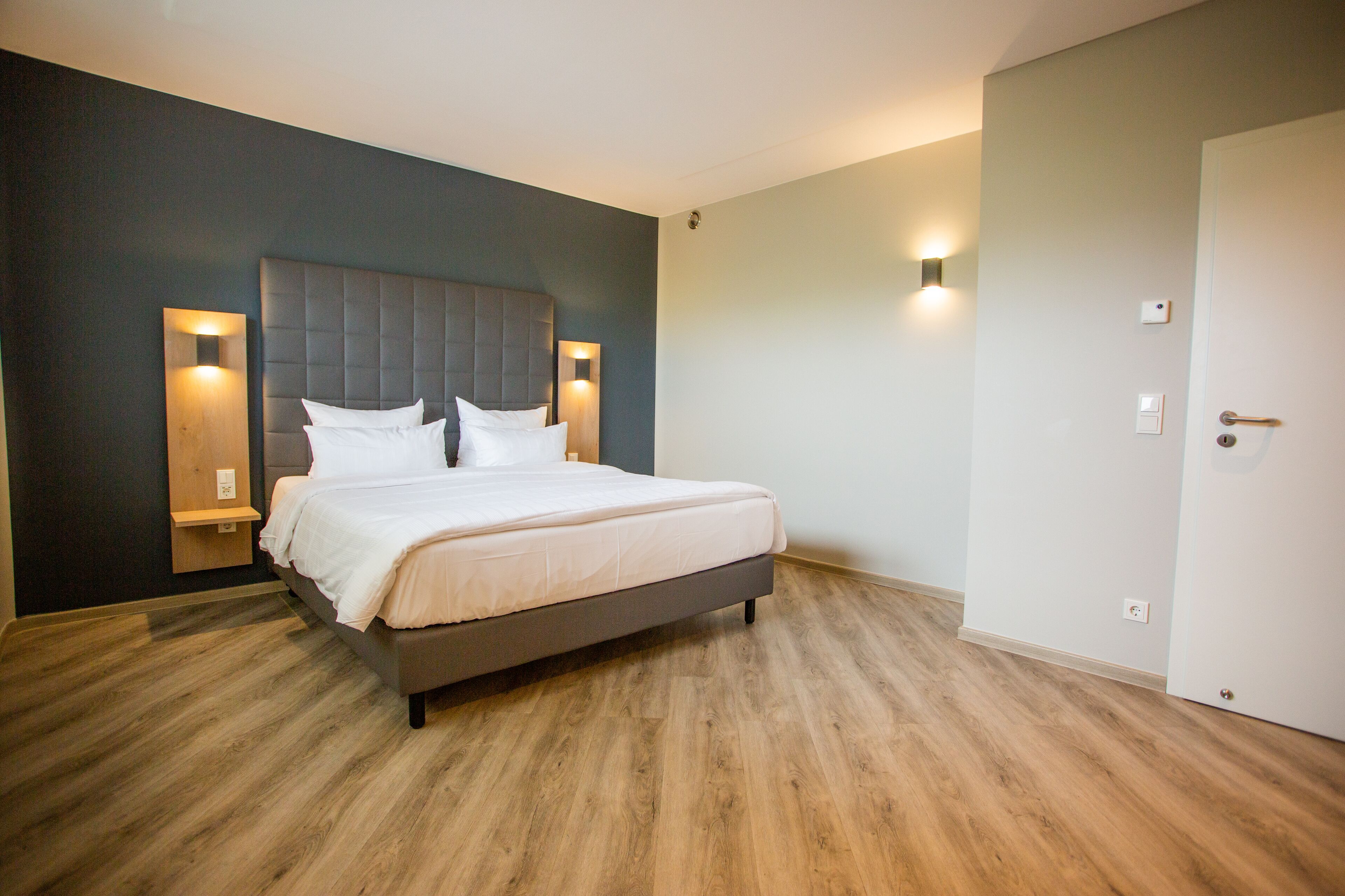 Un dormitorio moderno con una cama grande, suelo de madera e iluminación empotrada.