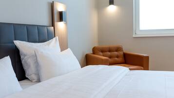 A hotel room with a large bed, a headboard, a brown leather armchair, and wall-mounted lighting.