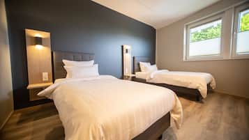 Une chambre d’hôtel avec deux lits, un mur sombre, une fenêtre et un plancher en bois.