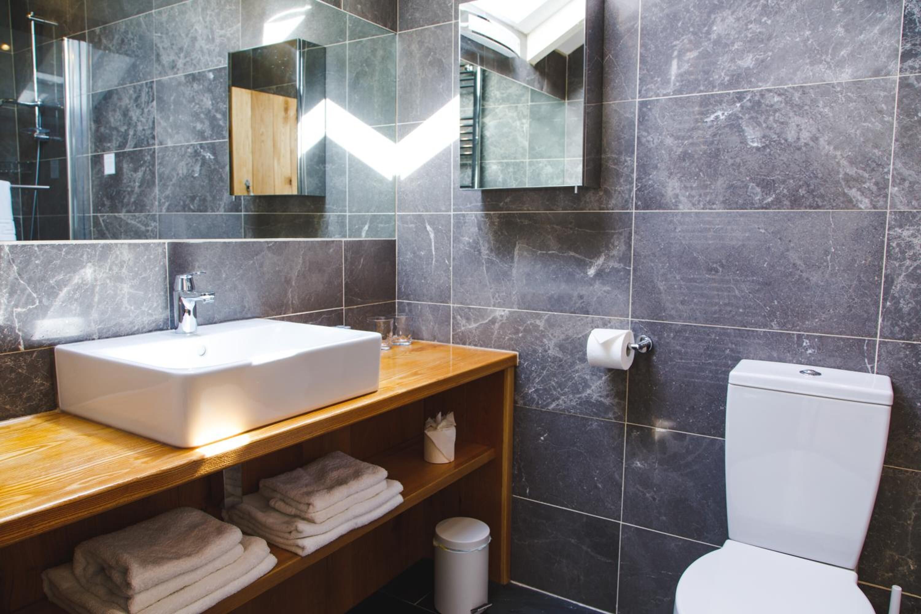 Een moderne badkamer met een marmeren wastafel, een houten wastafelmeubel en een toilet.